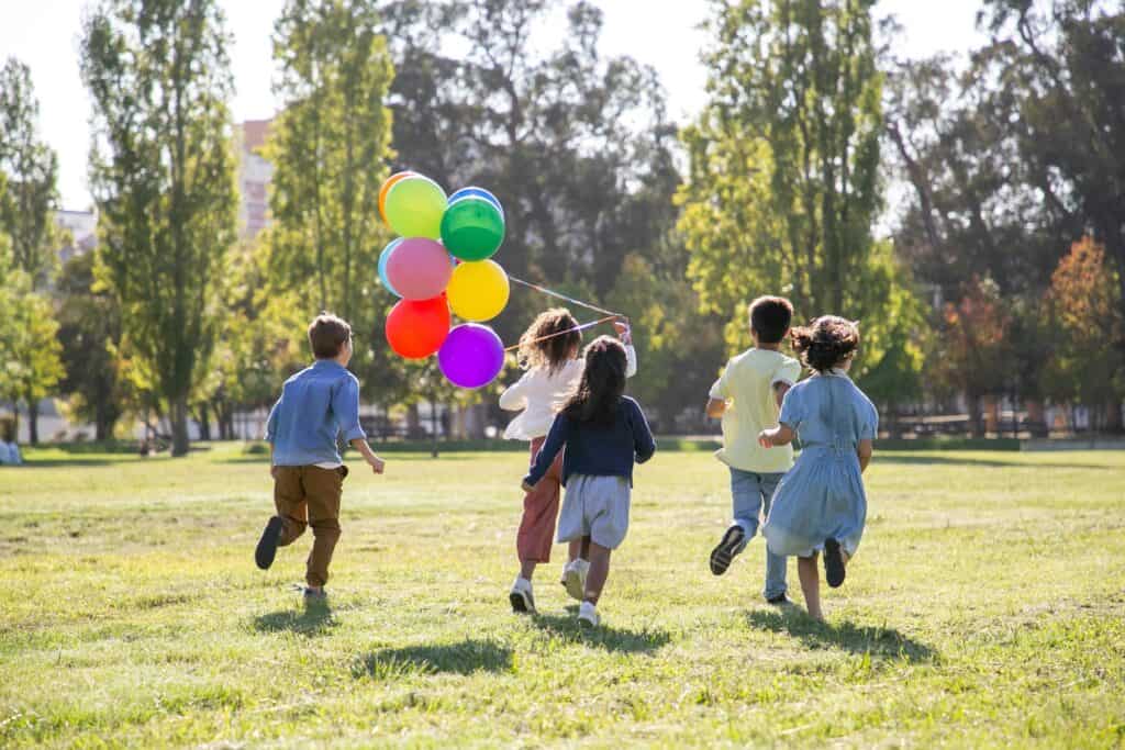 Kids running on the field holding balloons