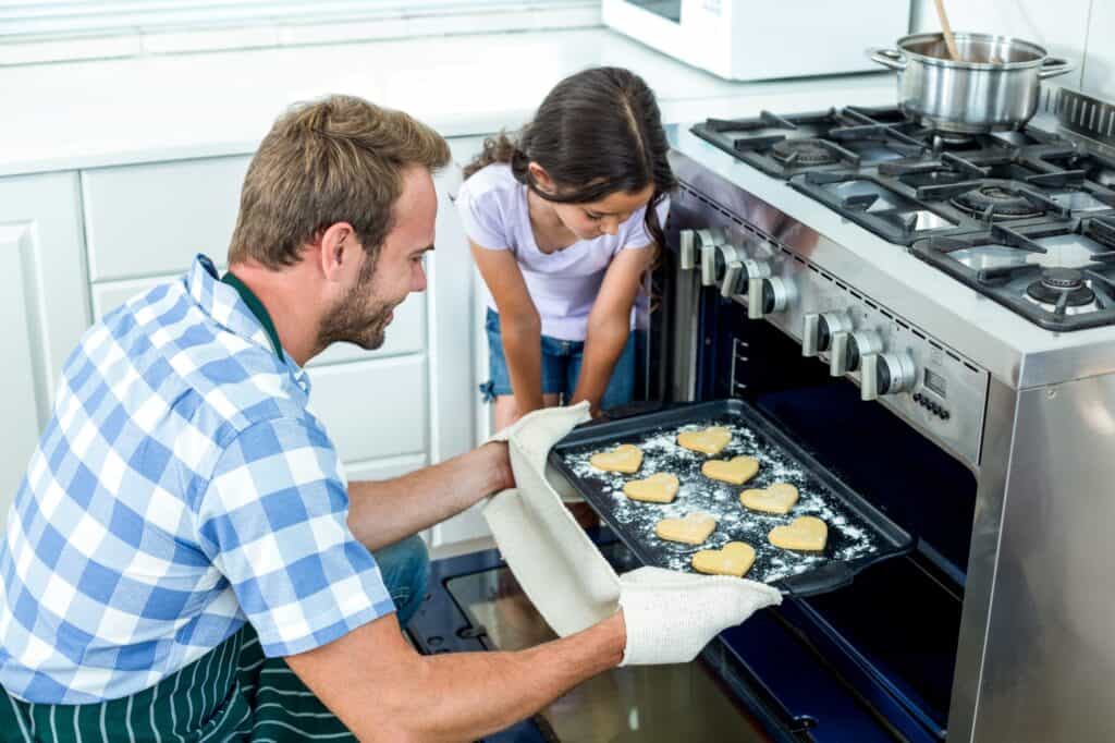 A father and daughter baking cookies in the oven