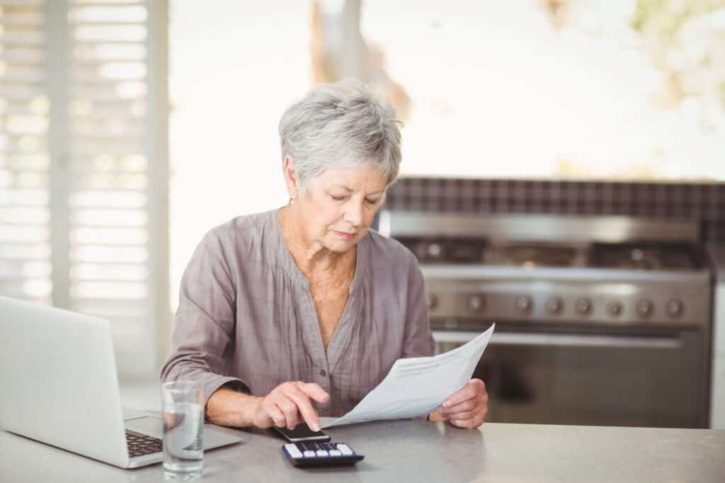 A senior lady in front of the computer, holding a paper, and using the calculator to compare man and van quotes